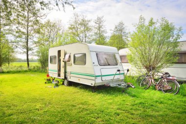 Kamp alanındaki yeşil çimlerde beyaz karavan karavanı. Güneşli bir gün. Bahar manzarası. Avrupa. Yaşam tarzı, seyahat, eko-turizm, yol gezisi, yolculuk, tatiller, eğlence, ulaşım, karavan, karavan