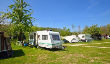 Kamp alanındaki yeşil çimlerde beyaz karavan karavanı. Güneşli bir gün. Bahar manzarası. Avrupa. Yaşam tarzı, seyahat, eko-turizm, yol gezisi, yolculuk, tatiller, eğlence, ulaşım, karavan, karavan