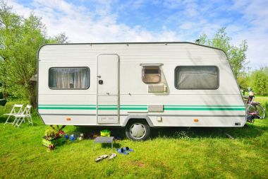 Kamp alanındaki yeşil çimlerde beyaz karavan karavanı. Güneşli bir gün. Bahar manzarası. Avrupa. Yaşam tarzı, seyahat, eko-turizm, yol gezisi, yolculuk, tatiller, eğlence, ulaşım, karavan, karavan