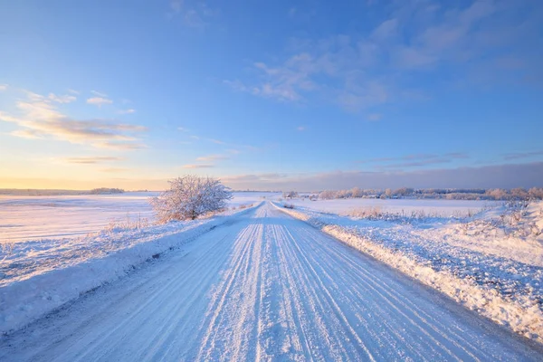 Estrada rural coberta de neve durante o pôr do sol de inverno — Fotografia de Stock