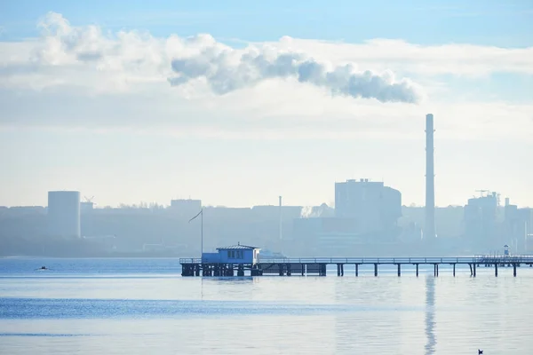 Seascape of a pier against a cityscape with a factory pipe — Stock Photo, Image