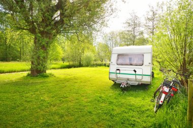 Kamp alanındaki yeşil çimlerde beyaz karavan karavanı. Güneşli bir gün. Bahar manzarası. Avrupa. Yaşam tarzı, seyahat, eko-turizm, yol gezisi, yolculuk, tatiller, eğlence, ulaşım, karavan, karavan