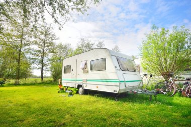 Kamp alanındaki yeşil çimlerde beyaz karavan karavanı. Güneşli bir gün. Bahar manzarası. Avrupa. Yaşam tarzı, seyahat, eko-turizm, yol gezisi, yolculuk, tatiller, eğlence, ulaşım, karavan, karavan