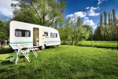 Kamp alanındaki yeşil çimlerde beyaz karavan karavanı. Güneşli bir gün. Bahar manzarası. Avrupa. Yaşam tarzı, seyahat, eko-turizm, yol gezisi, yolculuk, tatiller, eğlence, ulaşım, karavan, karavan