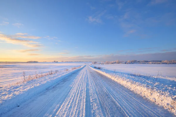 Estrada rural coberta de neve durante o pôr do sol de inverno — Fotografia de Stock