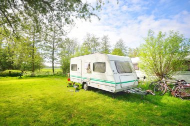 Kamp alanındaki yeşil çimlerde beyaz karavan karavanı. Güneşli bir gün. Bahar manzarası. Avrupa. Yaşam tarzı, seyahat, eko-turizm, yol gezisi, yolculuk, tatiller, eğlence, ulaşım, karavan, karavan