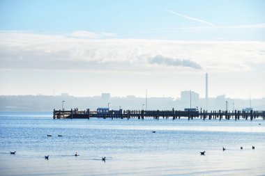 Bir fabrika boru ile cityscape karşı bir iskele, deniz manzarası