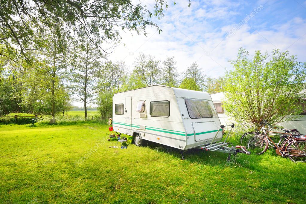 White caravan trailer on a green lawn in a camping site. Sunny day. Spring landscape. Europe. Lifestyle, travel, ecotourism, road trip, journey, vacations, recreation, transportation, RV, motorhome
