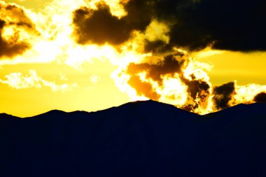 Parlayan sarı gün batımı inanılmaz bulutlar arasında muhteşem dağ siluetinin üzerinde.