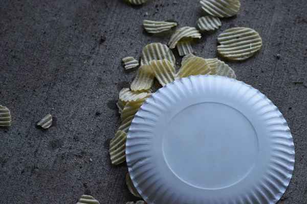 Sarı patates cipsli beyaz kağıt tabak döküldü ve beton desenli zemine döküldü.. 