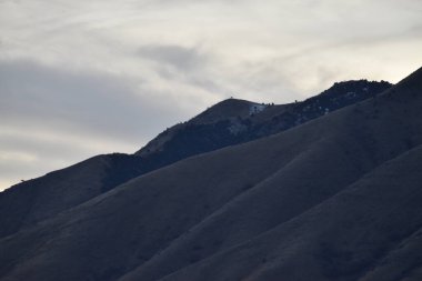 Karanlık, eğimli tepeler ve arka planda mavi ve beyaz bulutlar olan dağlar