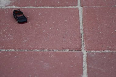 Beyaz harç harcı ile kırmızı fayanslı kaldırımlara park edilmiş küçük siyah ve kırmızı oyuncak bir araç.. 