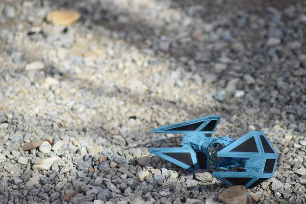 Çakıl taşlarının üzerinde yere serilmiş mavi uzay oyuncağı.