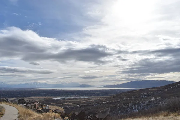 Güneş mavi gökyüzünde parlıyor, bulutlar, dağ, şehir ve uzak göl.