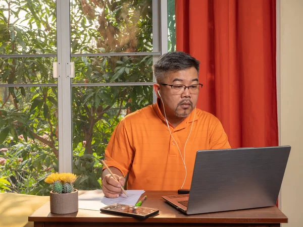 A businessman sitting and working through a laptop computer and headphones at home. Men working from home during the pandemic of the COVID-19. To prevent contact and maintain social distancing rules
