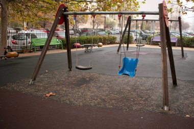 Kamu parkındaki renkli çocukların oyun alanı sonbahar ağaçlarıyla çevrili. Çocuklar oyun alanında koşuyor, kayıyor, salınıyor. Kentsel mahalle çocukluk kavramı.