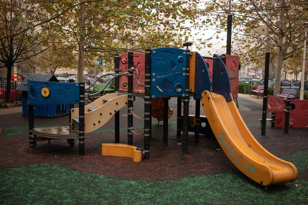 공원의 어린이 놀이터 의나무들 에둘러 어린이들이 달리고 미끄러져 운동장에서 주변의 스톡 사진