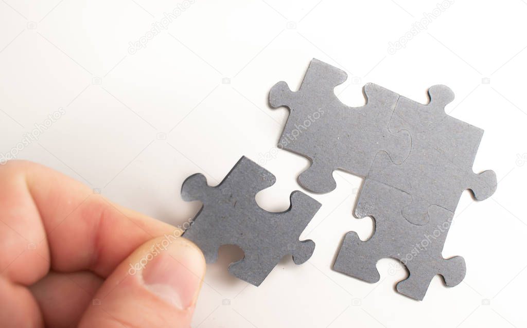 Human hand placing a piece of a puzzle, trying to solve it. Puzzle on background