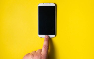 İnsan eli cep telefonunun tuşuna basıyor. Telefon sarı arka planda. Metin için boşluk.