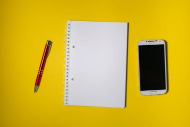 Kalem ve cep telefonu olan bir defterin üst görüntüsü. Metin için alanı olan renkli bir arkaplan üzerinde düz uzandı.