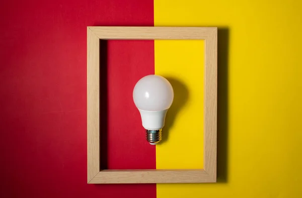 Wooden frame with a light bulb inside, on a colored background. Space for copy-paste. Top view of a rectangular frame