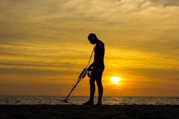 Cacciatore di tesori con metal detector al tramonto sulla spiaggia — Foto Stock