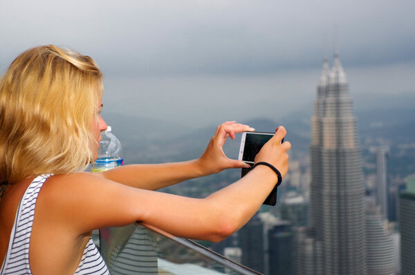 KUALA LUMPUR, MALAYSIA - January 17, 2016: Travel and technology. a Young woman taking photo with smartphone from KL- Tower at evening.
