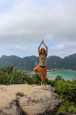 genç adam bir rock açık havada Phi Don Island, Tayland tarihinde yukarıdan Körfez Manzaralı lotus yoga poz ayakta.
