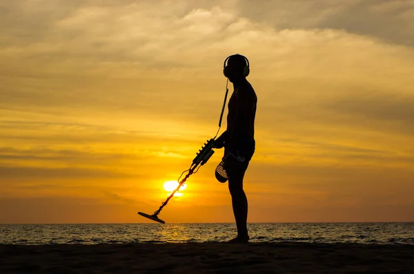 Caçador de tesouros com detector de metais ao pôr do sol na praia — Fotografia de Stock