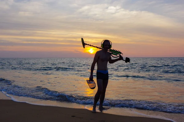 Caçador de tesouros com detector de metais ao pôr do sol na praia — Fotografia de Stock