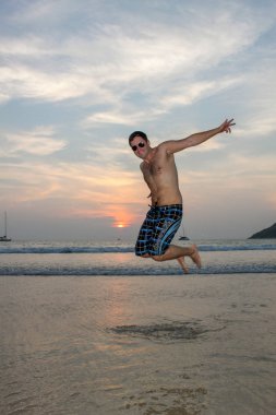 Adam arka planda günbatımı gökyüzü ile sahilde mutlu atlama