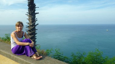 deniz kıyısı bir palmiye altında oturan ve sahil izlerken genç kadın