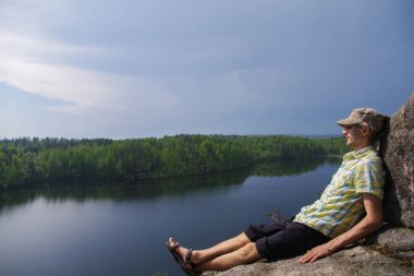göl üzerinde kayalık bir yamaçta oturan mutlu genç adam