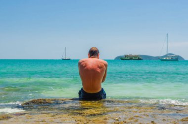 Genç adam kayalar ve denize bakarak oturur. Yalnızlık doğa yalnız ile rahatlayın. Zevk deniz manzarası ölçek kez.