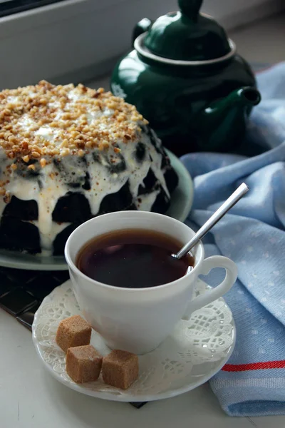 Pastel de chocolate decorado con migas de nuez y una taza de té caliente . — Foto de Stock