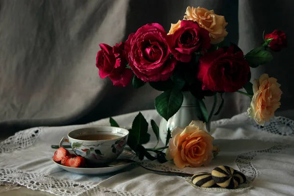 Una tazza di tè e biscotti contro un vaso con un mazzo di rose . — Foto Stock