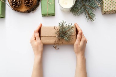 Kadın eli, Noel hediyeli bir kutuyu beyaz masada Noel süslemeleri ile birlikte tutuyor. Noel, Noel, Noel, kış, yeni yıl, sıfır atık kavramı. Düz konum, üst görünüm, kopyalama alanı, arkaplan.