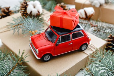 Çatıda kırmızı hediye kutusu olan kırmızı oyuncak araba. Pamuklu Noel arkaplanı, köknar dalları, köknar kozalakları. Noel tatili, kutlama, Noel, Noel, kış, yeni yıl konsepti.