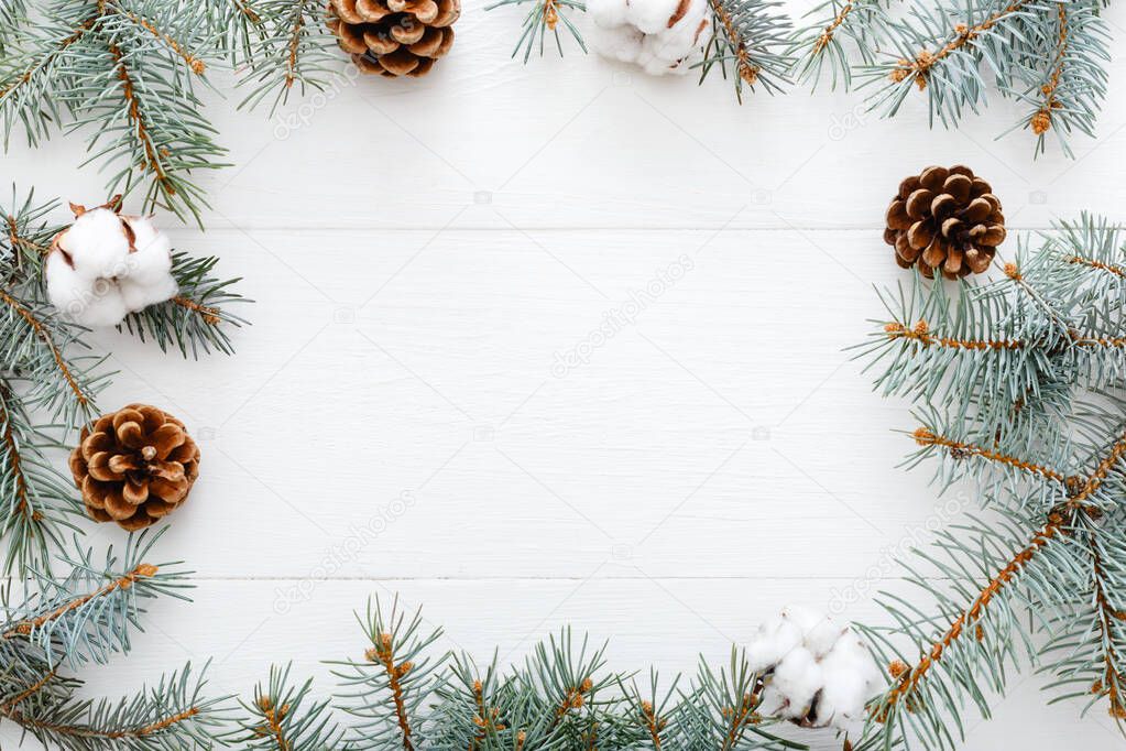Frame made of fir tree branches, cotton, bumps on white table background. Christmas composition. Christmas, Xmas, winter, new year concept. Flat lay, top view, copy space.