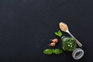 Cam kavanozda pesto sosu, çam fıstığı, yeşil fesleğen, koyu çimento üzerine sarımsak. Makarna, spagetti ve bruschetta için İtalyan pesto sosu. Üst görünüm, metin için kopyalama alanı olan düz uzanma
