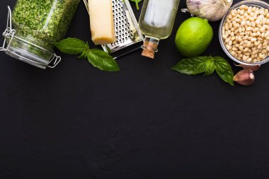 Cam kavanozda pesto sosu ve pesto sosu yapımında kullanılan malzemeler: çam fıstığı, yeşil fesleğen, koyu siyah çimento üzerine sarımsak. İtalyan pesto sosu. Üst manzara, çerçeve, düz yatış yeri metin için.