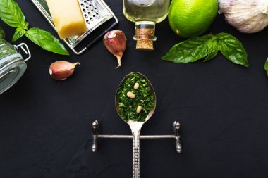 İçinde çam fıstığı, yeşil fesleğen, sarımsak, parmesan, koyu siyah çimento arkaplan üzerine zeytin yağı olan bir kaşık dolusu pesto sosu. Pesto sosu için İtalyan tarifi malzemeleri. Üst manzara, düz uzanma