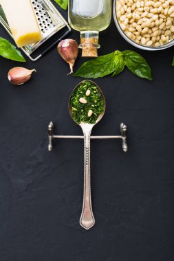 İçinde çam fıstığı, yeşil fesleğen, sarımsak, parmesan, koyu siyah çimento arkaplan üzerine zeytin yağı olan bir kaşık dolusu pesto sosu. Pesto sosu için İtalyan tarifi malzemeleri. Üst manzara, düz uzanma