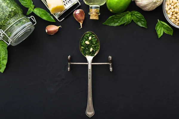 İçinde çam fıstığı, yeşil fesleğen, sarımsak, parmesan, koyu siyah çimento arkaplan üzerine zeytin yağı olan bir kaşık dolusu pesto sosu. Pesto sosu için İtalyan tarifi malzemeleri. Üst manzara, düz uzanma