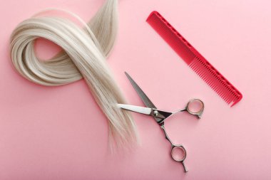 Kuaför aletleri, makas, tarak ve sarı saç teli ile düz konum pembe renk arka plan üzerinde metin için kopyalama alanı ile. Kuaför servisi. Güzellik salonu servisi..