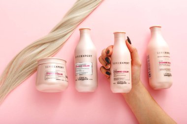 L 'oreal Profesnel Paris Serie Uzmanı Vitamino Renkli Saç Rengi Profesyonel Ürünleri seti. Pembe arka planda sarı saç teli. Pembe kozmetik şişeleri. Düz metin kopyalama alanı