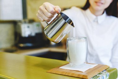 Kahveli latte yapma süreci. Beyaz tişörtlü genç, güzel bir kadın bir kafede Latte yapıyor, kafe, bar. Çift duvarlı bir bardak.