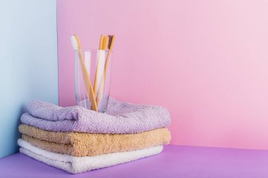 Biyo-çözünür doğal bambu diş fırçası. Camın içinde. Pastel renklerde pamuk havlular, pembe arka planda. Çevre dostu, sıfır atık diş bakımı Plastiksiz hijyensiz Kumaş Tekstil konsepti