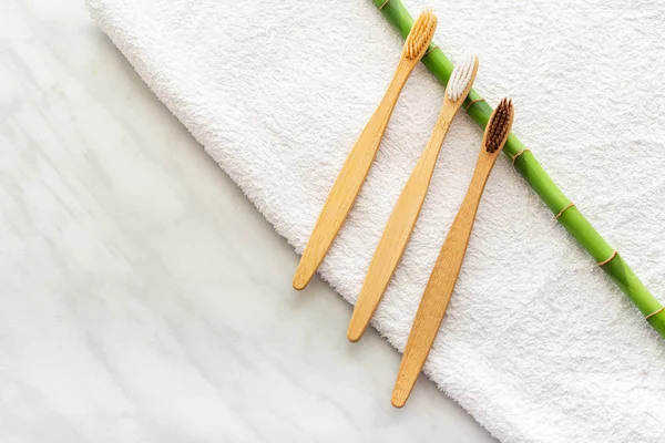 Bambu diş fırçaları, beyaz havluyla bambu bitkisi, mermer arka plan. Düz yatıyordu. Doğal banyo ürünleri. Biyolojik çözünür doğal bambu diş fırçası. Çevre dostu, sıfır atık, diş bakımı plastiksiz kavram.