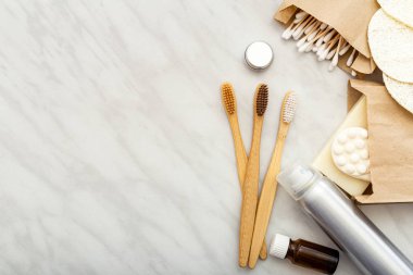 Sıfır atık doğal banyo ürünü. Bambu diş fırçaları, sabun pamuğu çubukları, beyaz mermer zemin üzerindeki lif bezleri. Düz kopya alanı. Çevre dostu, sıfır atık, plastik diş bakımı.